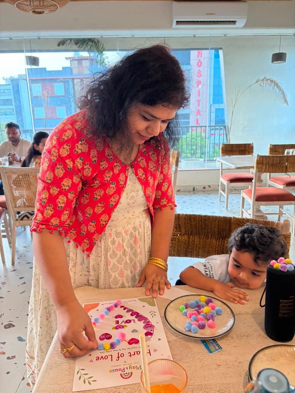 A mom and her toddler decorating a Play & Pause Heart of Love activity card with colourful pom-poms