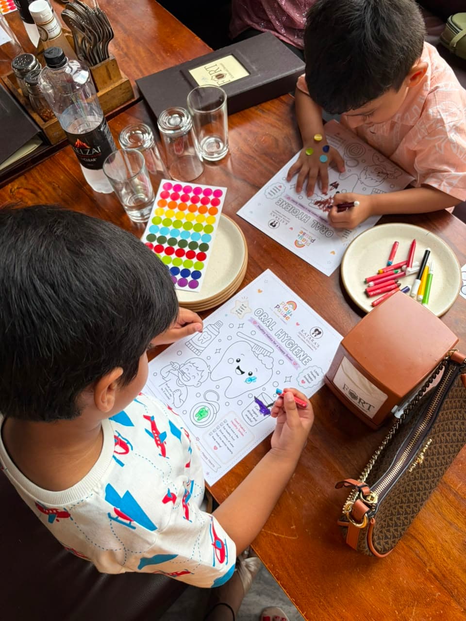 Two boys colouring their Play & Pause oral-hygiene sheets with sticker dots