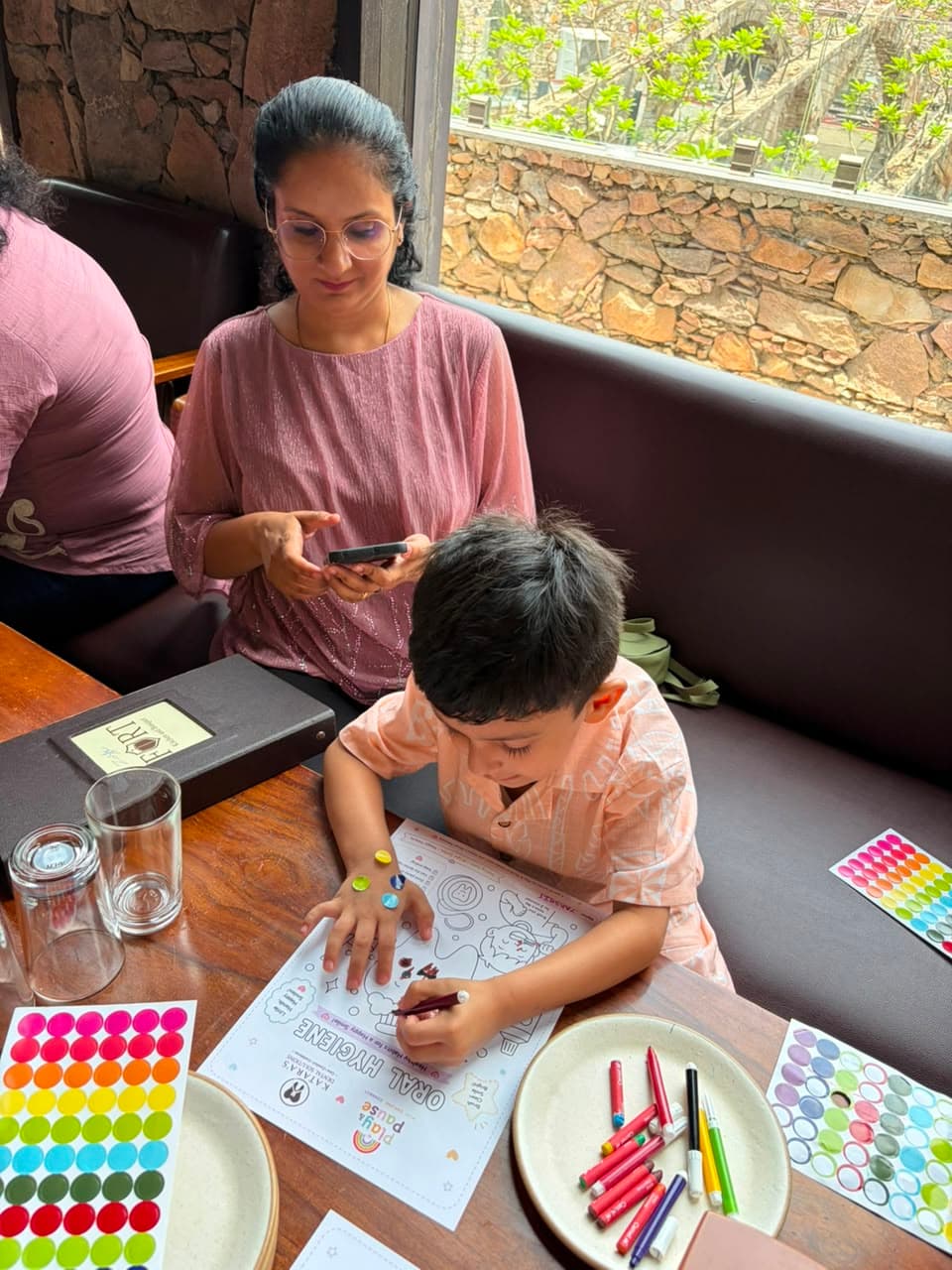 A little one colouring an activity sheet while his mom looks on at a Play & Pause session